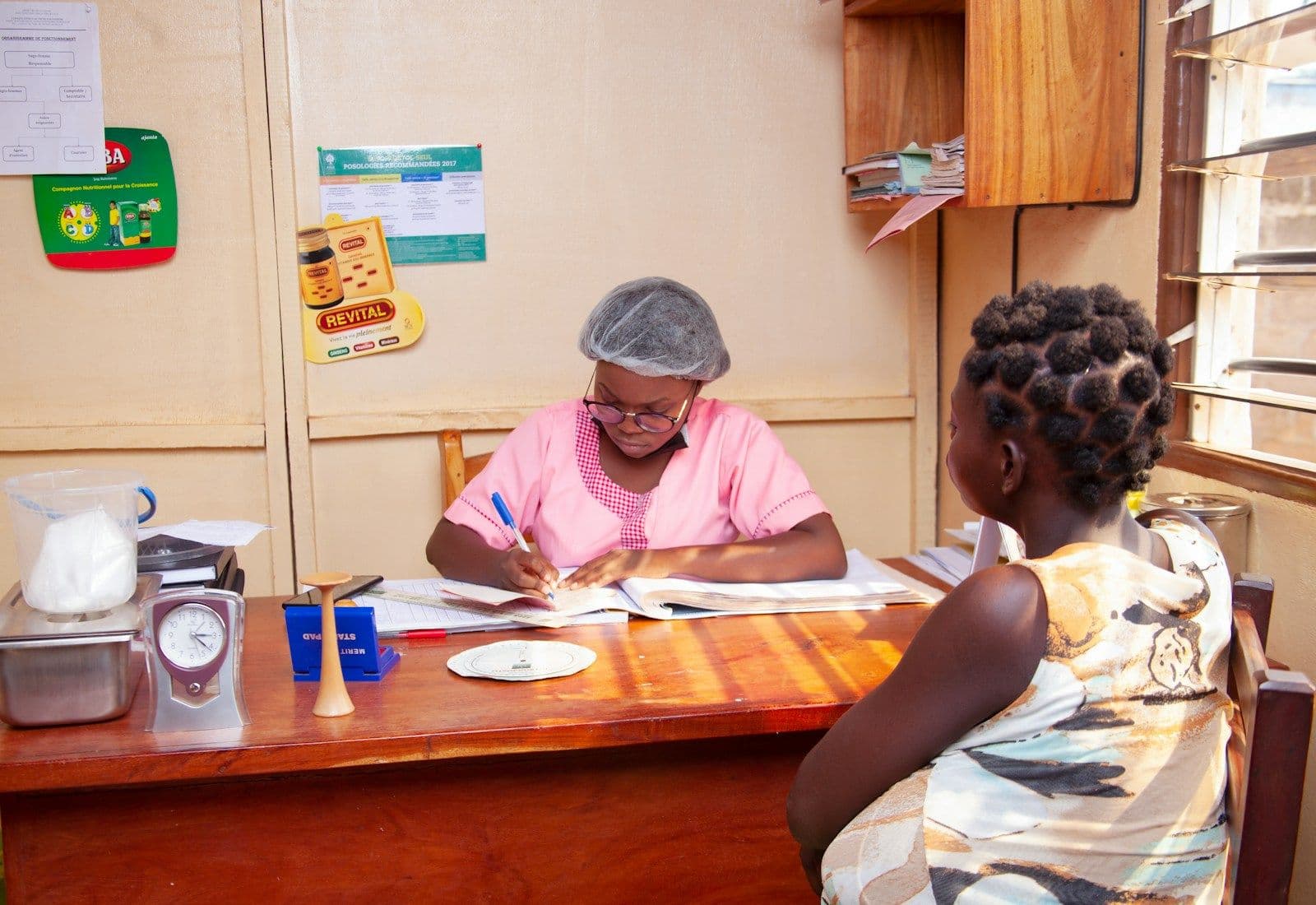 A clinic administrator filling in paper records while a patient waits
